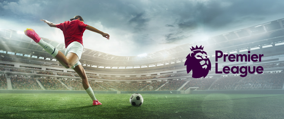 A football player in a red shirt and white shorts strikes the ball inside a large stadium, preparing to take a powerful kick. The sky is overcast, adding intensity to the atmosphere. The Premier League logo is displayed on the right side of the image, symbolising the energy and action of a Premier League match.