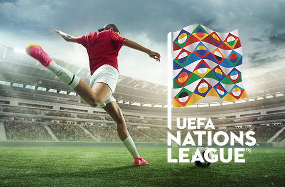 A football player in action on the field, kicking a ball in front of a stadium, with the UEFA Nations League flag displayed prominently in the foreground.