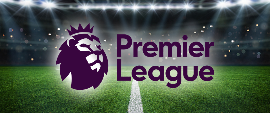 The image displays the Premier League logo featuring a purple lion's head alongside the "Premier League" text in bold. The background shows an illuminated football stadium with bright floodlights casting light onto the pitch. The view is from the centre of the pitch, creating a vibrant atmosphere of anticipation for a Premier League match.