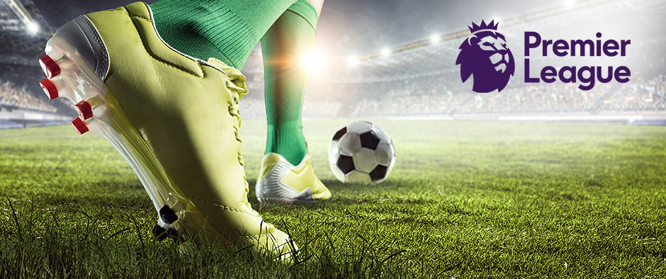 Close-up of a football player’s boots as they prepare to kick a soccer ball on a stadium field, with the Premier League logo displayed on the right against a backdrop of stadium lights.