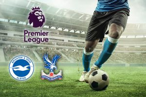 A football player in blue kit dribbles a ball on a pitch in a stadium. The Premier League logo and the Brighton & Hove Albion and Crystal Palace club logos are displayed.