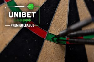 Close-up image of a dartboard showing three darts tightly grouped in the green triple section. The Unibet Premier League logo is prominently displayed in the upper left corner, featuring a green dart graphic and the company's name. The background highlights the texture of the dartboard segments, emphasizing the precision of the dart throws.