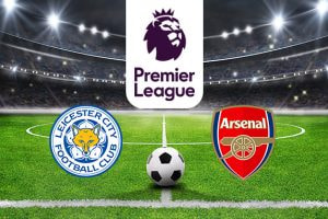 A football stadium under bright floodlights illuminating the pitch. At the centre is the Premier League logo above a soccer ball, with the Leicester City Football Club logo on the left and the Arsenal Football Club logo on the right, representing their upcoming match.