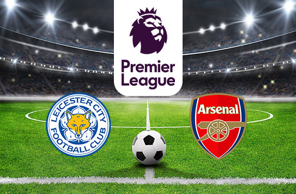 A football stadium under bright floodlights illuminating the pitch. At the centre is the Premier League logo above a soccer ball, with the Leicester City Football Club logo on the left and the Arsenal Football Club logo on the right, representing their upcoming match.